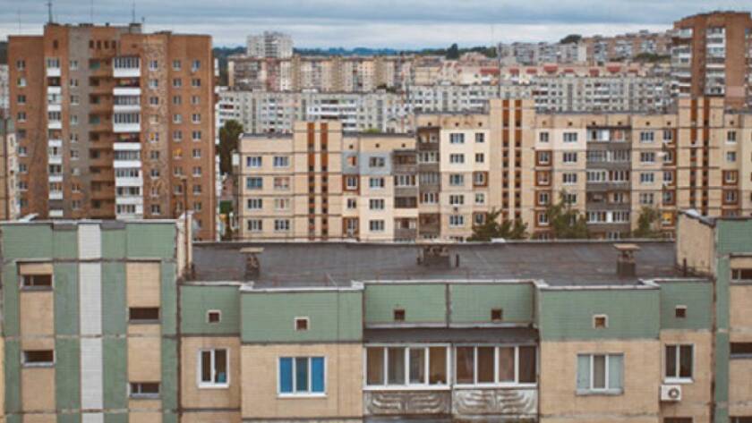 Row of green and beige apartment buildings in a dense urban neighborhood, with taller blocks in the background.