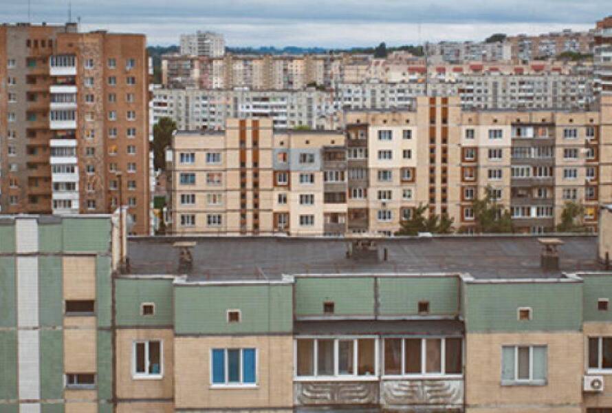 Row of green and beige apartment buildings in a dense urban neighborhood, with taller blocks in the background.