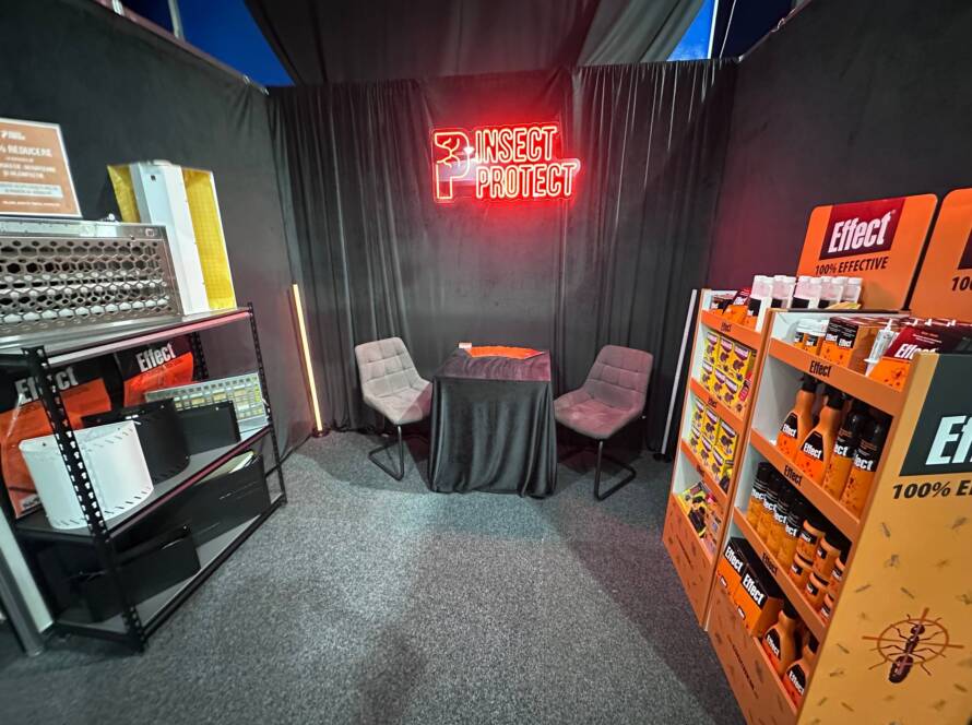 Booth corner with black drapes, a red neon 'INSECT PROTECT' sign, and two gray chairs around a small table.